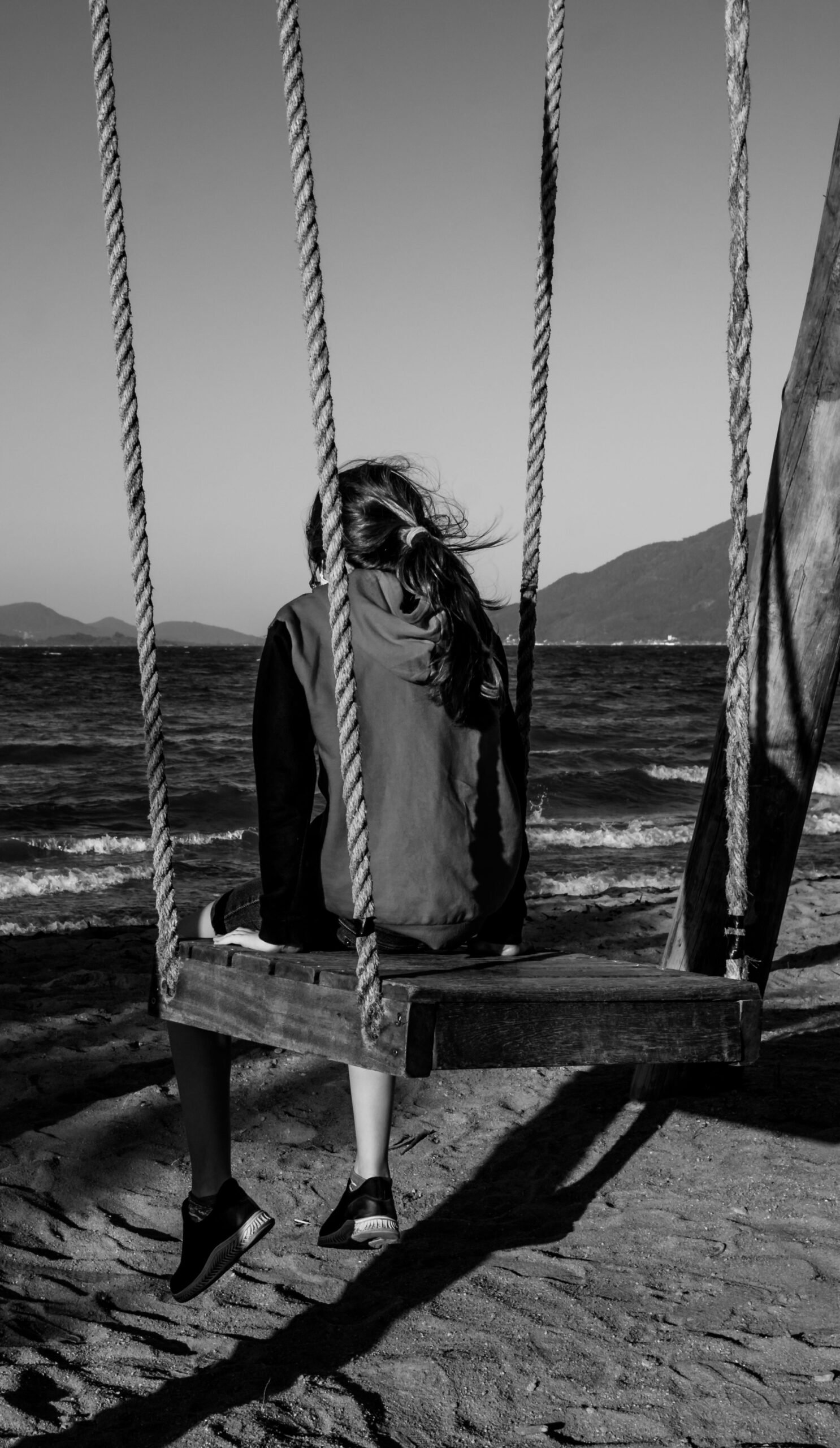 A person sitting on a swing by the ocean, black and white photography capturing solitude.