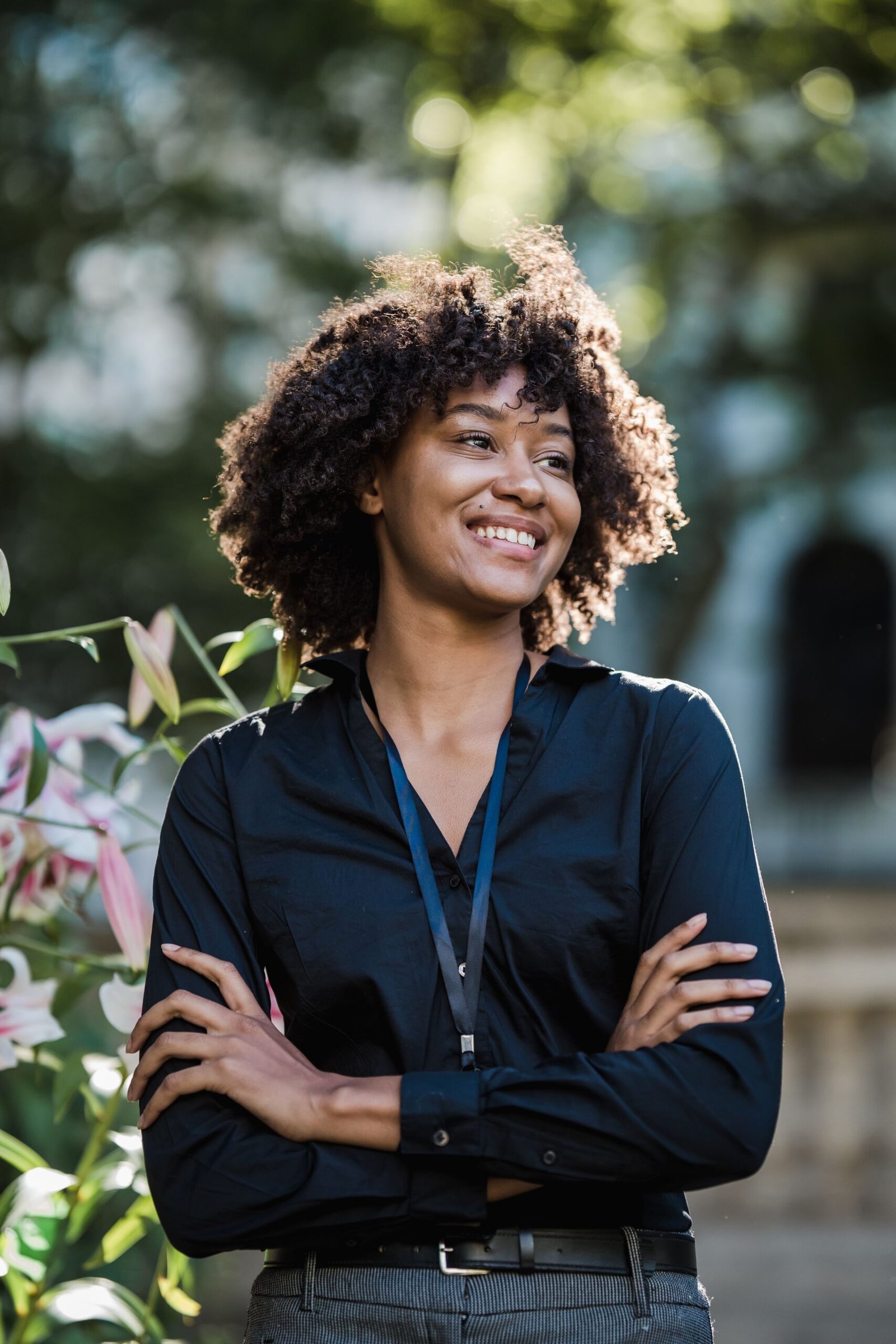 Confident woman smiling outdoors with crossed arms in a natural setting.